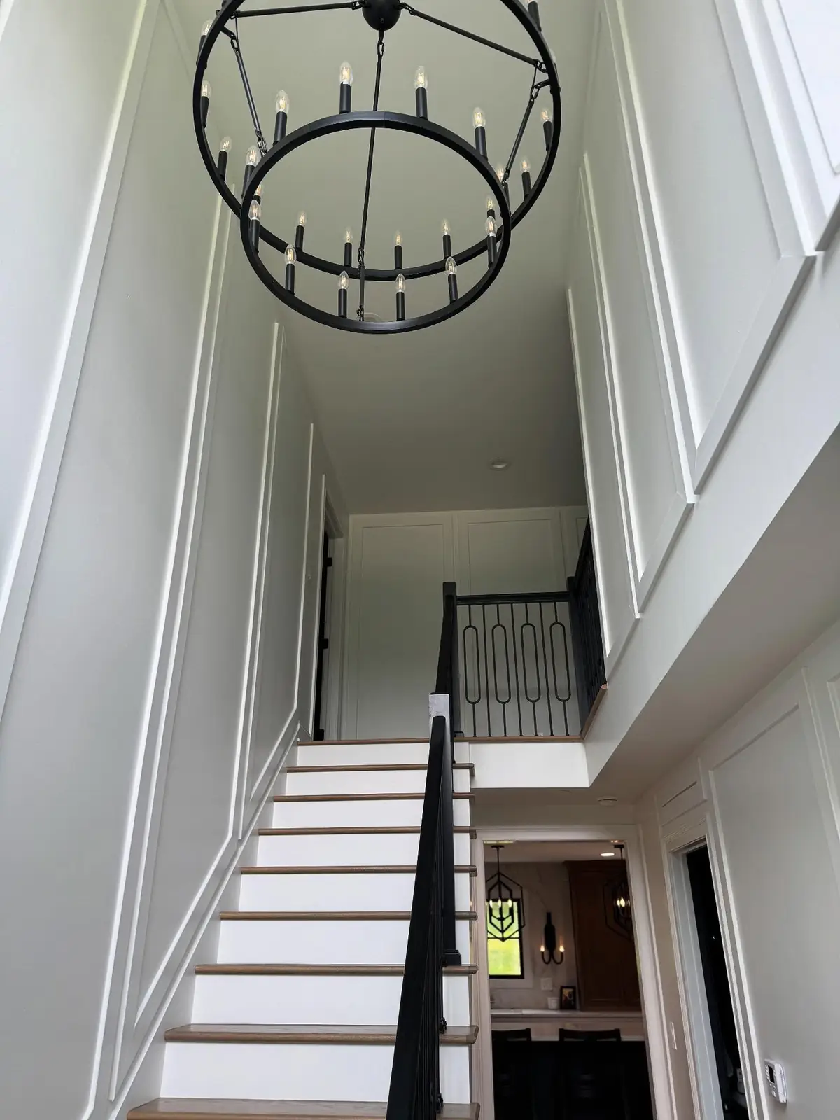 Staircase with black railing beneath an iron chandelier