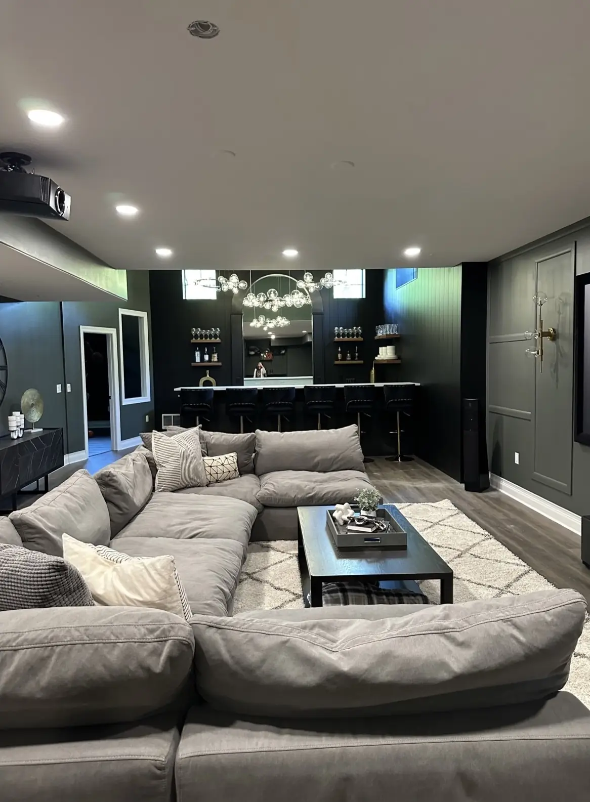 Lower level with a deep sectional and a bar beneath a glass-globe chandelier — Brookstone