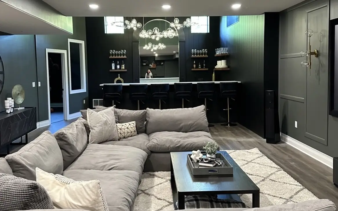Brookstone lower level: a deep sectional facing a black-paneled bar beneath a glass-globe chandelier
