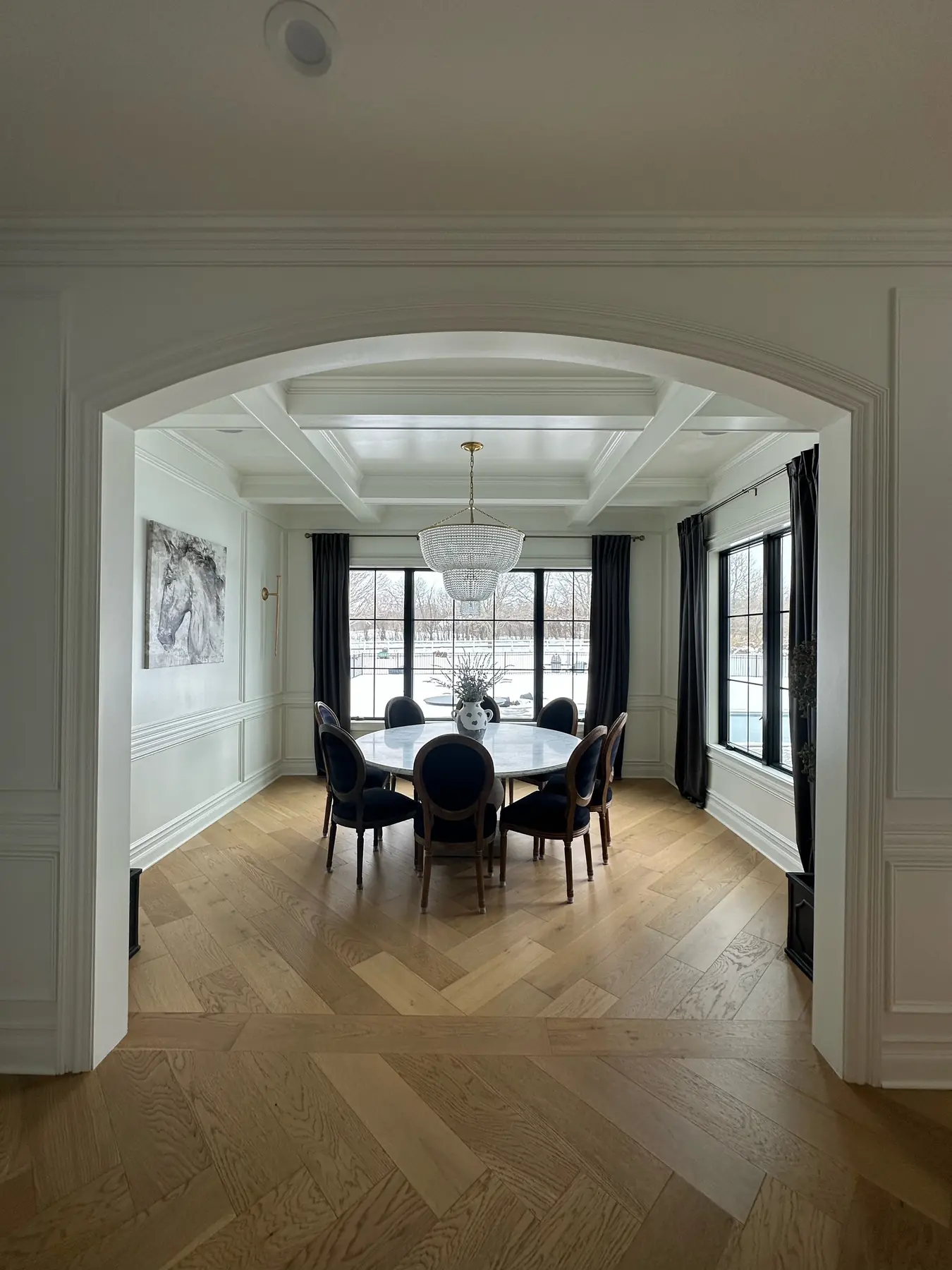 Dining room framed by an arched opening, beneath a coffered ceiling and crystal chandelier