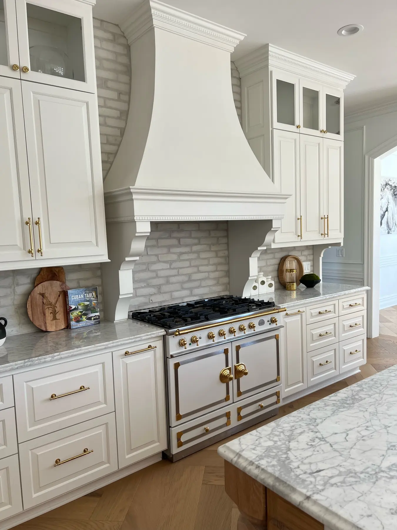 Kitchen in the French-Inspired Residence: a sculpted plaster range hood over a brick backsplash and brass-trimmed range