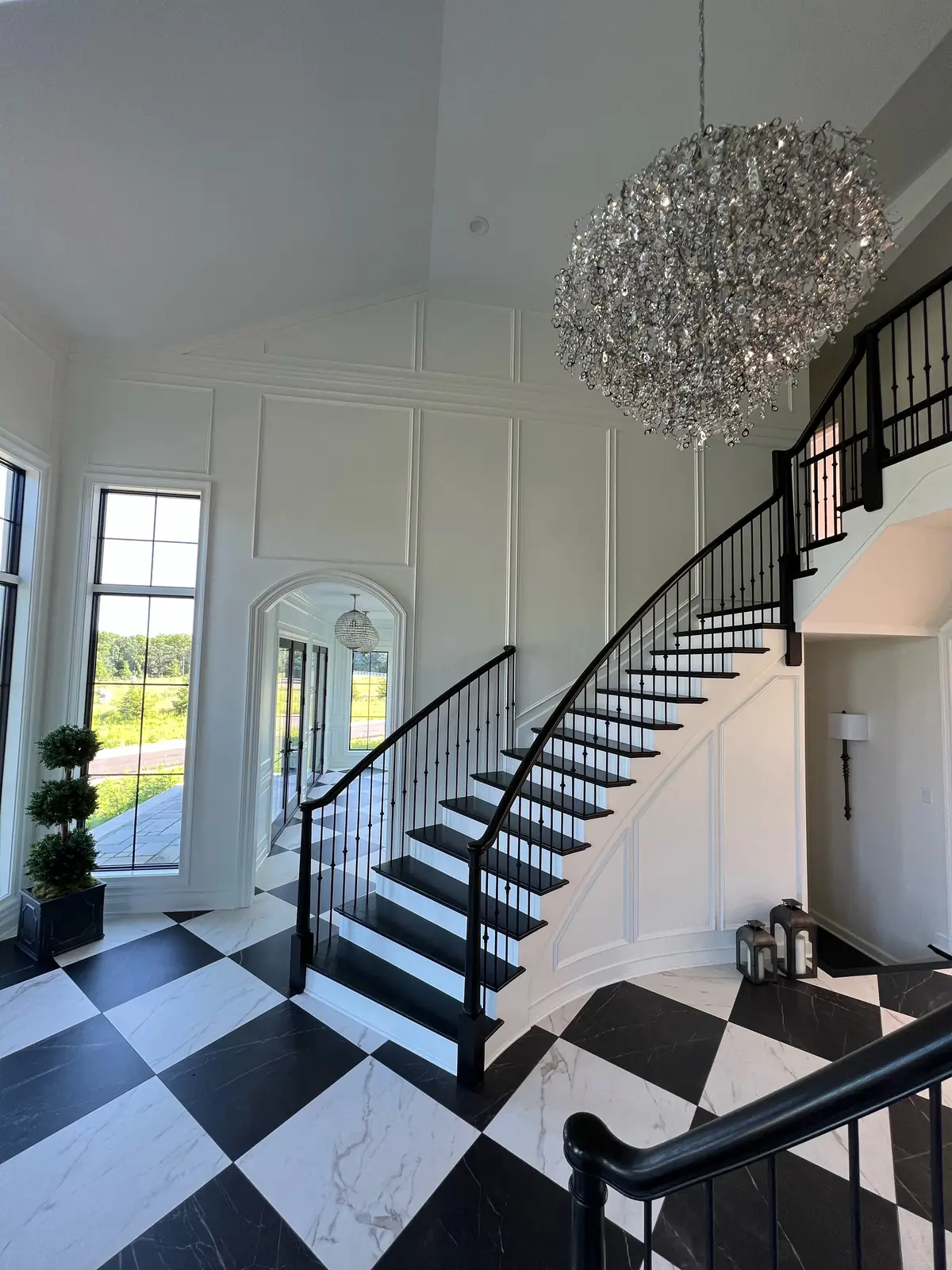 The curved stair beneath the crystal chandelier, with a topiary at its foot