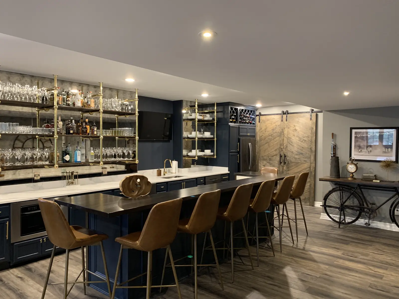 Bar after — navy cabinetry, brass shelving and leather stools