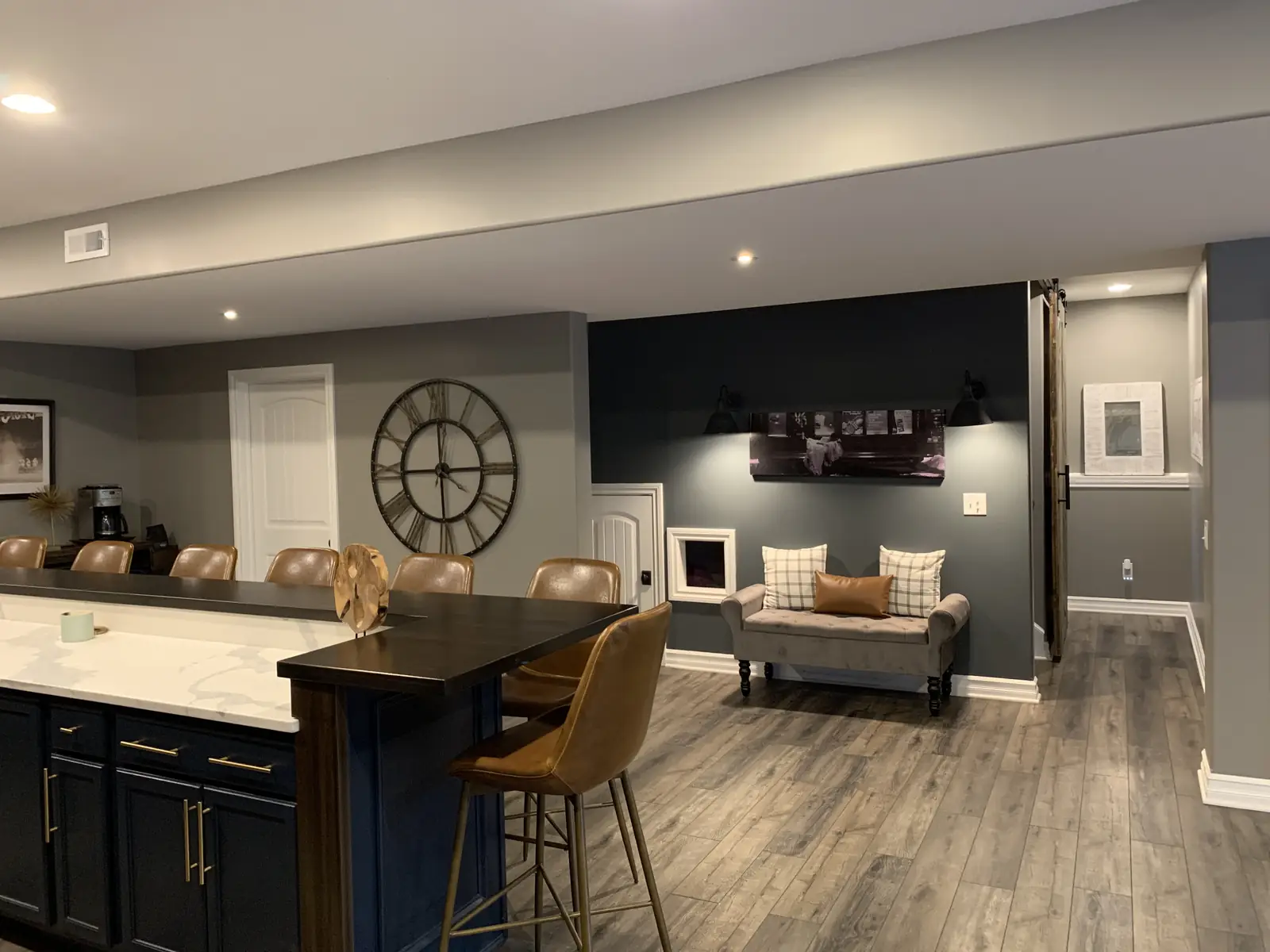 The end of the bar, a large clock and a navy accent wall with a bench
