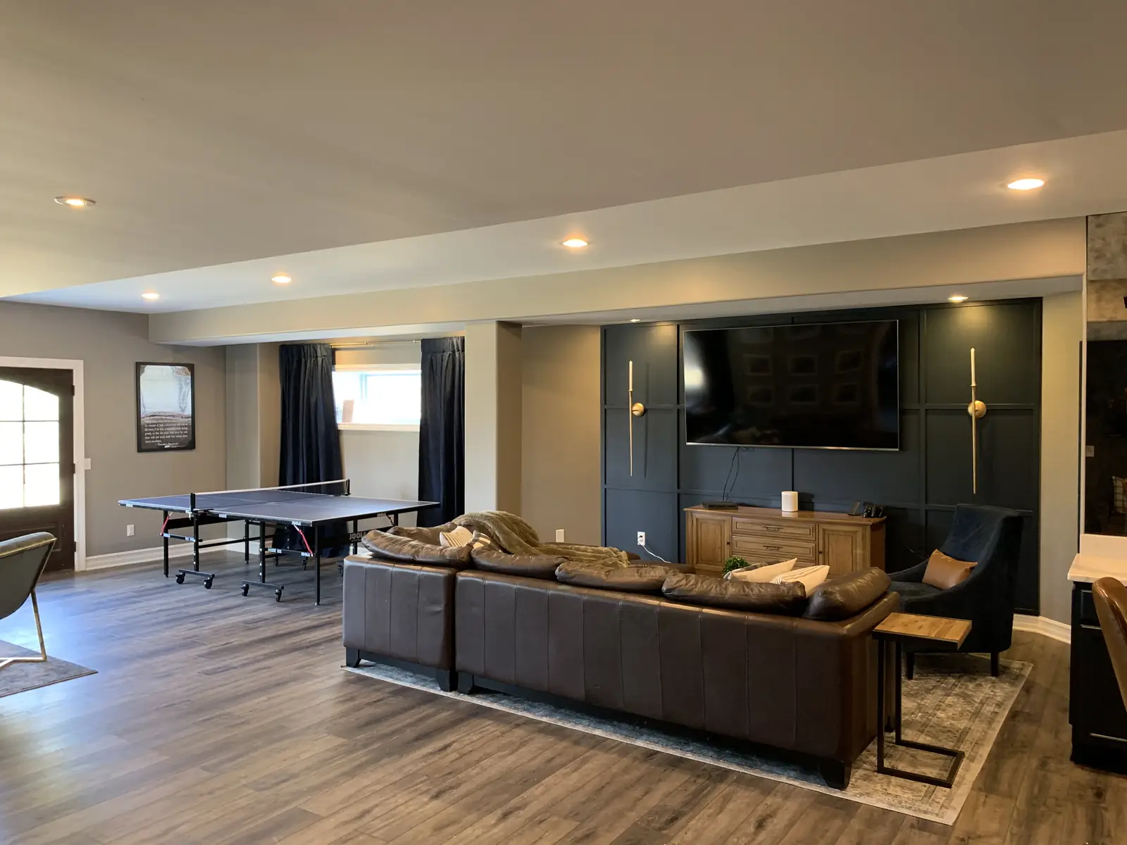 TV wall after — navy paneling, a sectional and a ping-pong table